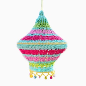 May include: A colorful crocheted lampshade with a striped pattern in shades of pink, green, blue, and yellow. The lampshade has a fringe trim with colorful beads.