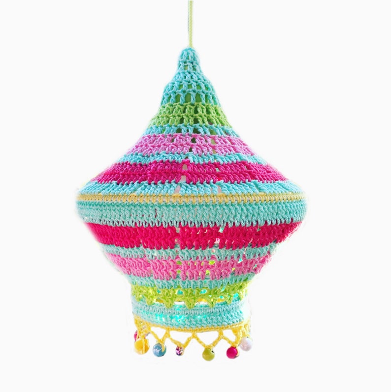 May include: A colorful crocheted lampshade with a striped pattern in shades of pink, green, blue, and yellow. The lampshade has a fringe trim with colorful beads.
