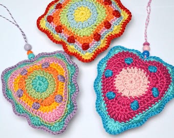 May include: Three heart-shaped crochet ornaments featuring vibrant, multi-colored yarn patterns. Each piece includes a scalloped edge, raised circular accents, and a hanging string adorned with small, colorful wooden beads in various shades.