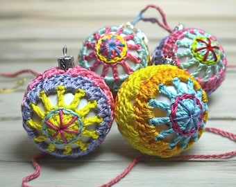 May include: Four spherical ornaments covered in intricate, multi-colored crochet patterns. Each ornament features a white base layer visible through the yarn work, with vibrant hues of yellow, pink, light blue, and lavender arranged in geometric designs.
