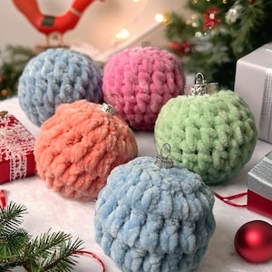 以下が含まれることがあります： ピンク、青、オレンジ、緑の色合いの、6つのカラフルなぬいぐるみクリスマスオーナメントのコレクション。各オーナメントには、吊り下げ用のシルバーキャップとループが付いています。オーナメントは、クリスマスツリーやその他の装飾が背景にある白い表面に配置されています。