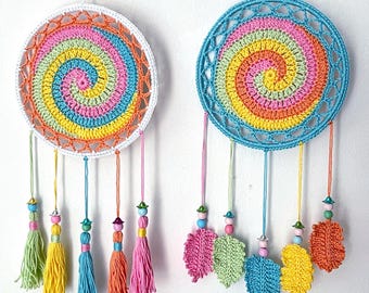May include: Two circular wall hangings featuring a crocheted spiral pattern in pink, yellow, orange, and light blue. The left piece has a white frame with five colorful yarn tassels, while the right piece has a blue frame with five crocheted leaf-shaped pendants.