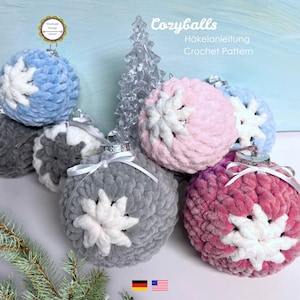 May include: A collection of plush, crocheted Christmas ornaments in various colors, including blue, pink, gray, and burgundy. Each ornament features a white starburst design. The image also includes text that reads "Cozyballs" and "Crochet Pattern".