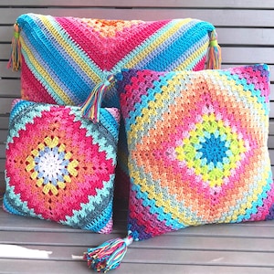 Könnte beinhalten: Drei bunte gehäkelte Kissen mit Fransen. Die Kissen sind in verschiedenen leuchtenden Farben gehalten, darunter Pink, Blau, Gelb und Grün.