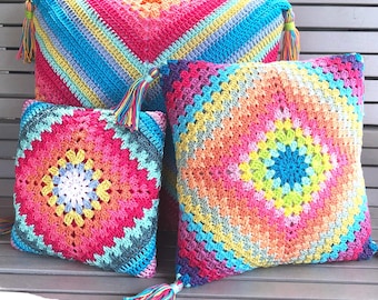 May include: Three square and rectangular throw pillows featuring a vibrant, multi-colored crochet granny square pattern. The pillows display concentric diamond designs in shades of pink, blue, yellow, orange, and purple, finished with decorative tassels.
