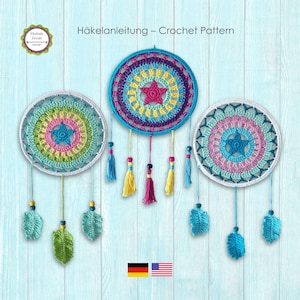 Könnte beinhalten: Drei farbenfrohe Häkel-Traumfänger mit Sternen in der Mitte und Quastenakzenten hängen vor einem hellblauen Holzmaserungshintergrund. Die Traumfänger weisen konzentrische Kreise in Blau-, Rosa-, Gelb- und Grüntönen auf. Der Text "Häkelanleitung - Crochet Pattern" steht oben.