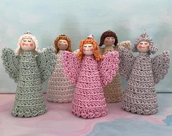 May include: Five handmade crochet angel figurines with wooden bead heads, painted faces, and yarn hair. Each angel features a textured dress and wings in various colors including sage green, cream, pink, beige, and grey, topped with a small silver loop.