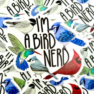 May include: A white sticker with the text "I'm a bird nerd" in black. The sticker features illustrations of five different birds: a blue jay, a hummingbird, a cardinal, a chickadee, and a black-capped chickadee.