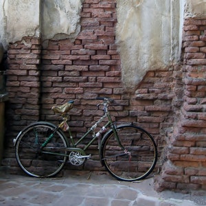 May include: A green bicycle is parked against a brick wall. The bicycle has a brown leather saddle and a basket on the handlebars.