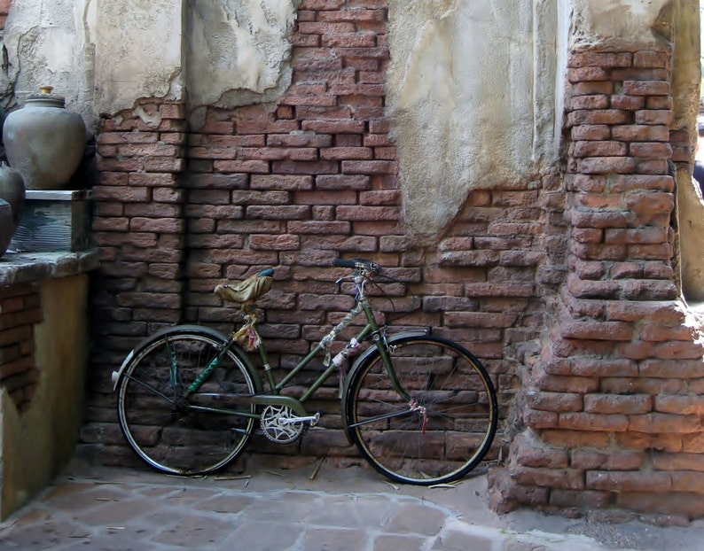 May include: A green bicycle is parked against a brick wall. The bicycle has a brown leather saddle and a basket on the handlebars.