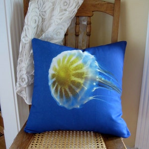 May include: A blue pillow with a white and yellow jellyfish design. The pillow is sitting on a wooden chair with a woven seat.