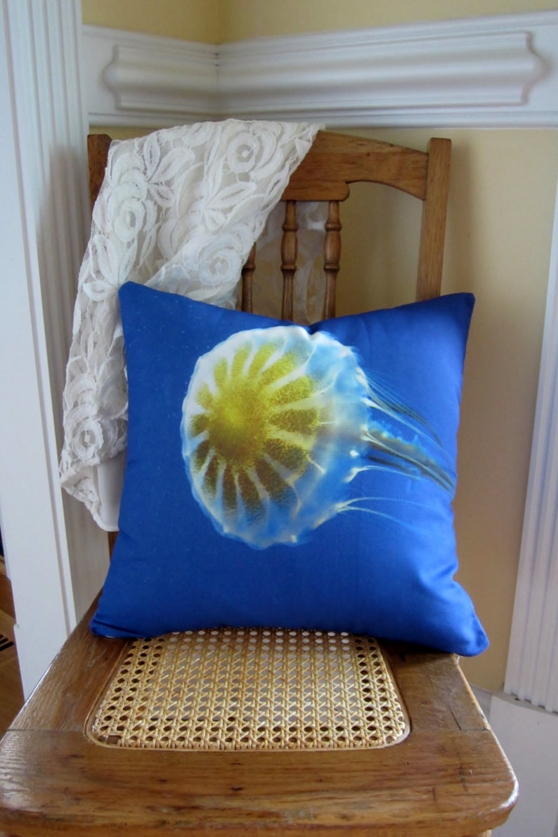 May include: A blue pillow with a white and yellow jellyfish design. The pillow is sitting on a wooden chair with a woven seat.