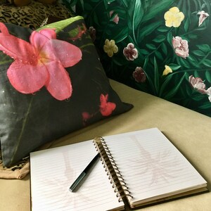 Puede incluir: Una almohada floral en blanco y negro con una flor rosa en un sof&aacute; con un cuaderno y un bol&iacute;grafo encima. El sof&aacute; est&aacute; frente a una pared verde con un patr&oacute;n floral.