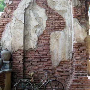 May include: A vintage-style bicycle with a brown leather saddle and rust-coloured handlebars is parked against a brick wall with white plaster. The wall is weathered and has a rustic look.
