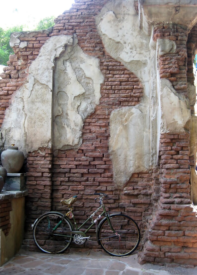 May include: A vintage-style bicycle with a brown leather saddle and rust-coloured handlebars is parked against a brick wall with white plaster. The wall is weathered and has a rustic look.