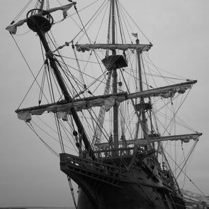 Puede incluir: Una fotograf&iacute;a en blanco y negro de un gran barco de vela de madera con m&uacute;ltiples m&aacute;stiles y velas. El barco est&aacute; atracado en un muelle y el agua est&aacute; tranquila.