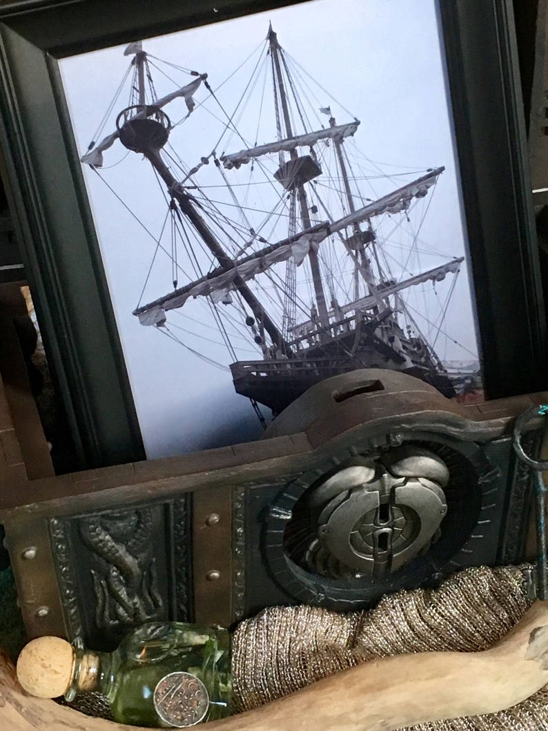 Puede incluir: Una fotograf&iacute;a en blanco y negro enmarcada de un barco alto con velas, sobre un fondo de madera con una pieza de metal decorativa y una botella de l&iacute;quido verde con un tap&oacute;n de corcho.