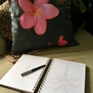 Puede incluir: Un diario negro y blanco con encuadernaci&oacute;n en espiral, un bol&iacute;grafo negro y una almohada de flores rosas con un dise&ntilde;o de hojas verdes.