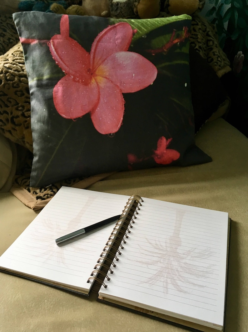 Puede incluir: Un diario negro y blanco con encuadernaci&oacute;n en espiral, un bol&iacute;grafo negro y una almohada de flores rosas con un dise&ntilde;o de hojas verdes.