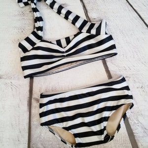 May include: Black and white striped bikini top and bottom. The top has a halter style with a bow tie at the neck. The bottom is a high-waisted style.