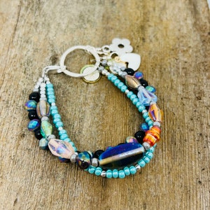 May include: A multi-strand bracelet with turquoise, black, and iridescent beads. The bracelet has a silver clasp and charm.
