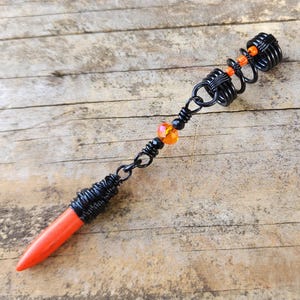 Op de afbeelding: Een zwarte en oranje haarspiraal met een rood en zwart parel uiteinde.