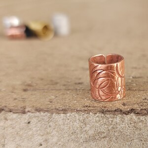 May include: A copper ring with a decorative etched design. The ring is a cylinder shape and has a smooth, polished finish.
