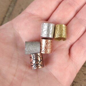 May include: Five decorative metal hair cuffs in different colors and patterns. The cuffs are silver, gold, copper, and black.