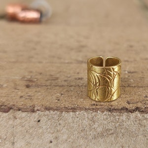 May include: A gold-toned ring with a textured, patterned design. The ring is open on one side and has a slightly curved shape.