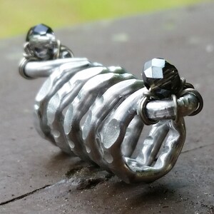 May include: A silver metal ring with a textured, rib-like design. The ring is decorated with two black gemstones.