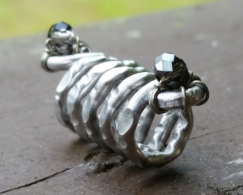 May include: A silver metal ring with a textured, rib-like design. The ring is decorated with two black gemstones.