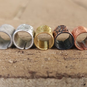 May include: Five metal rings with decorative patterns in silver, gold, black, and copper.