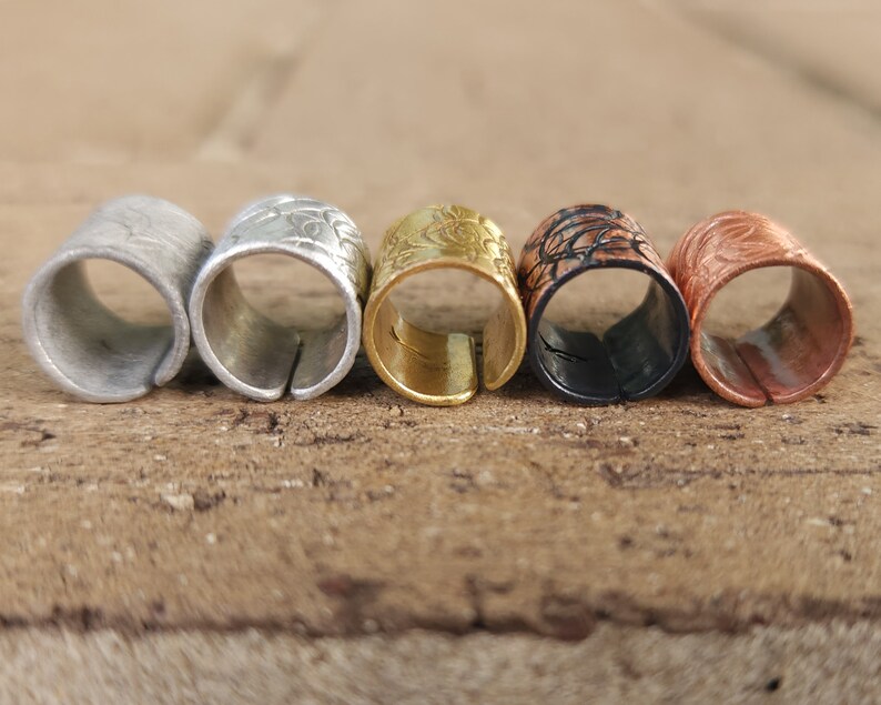 May include: Five metal rings with decorative patterns in silver, gold, black, and copper.