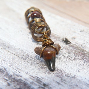 May include: A brown and gold shark tooth pendant with wire wrapped beads. The pendant is on a white wooden surface.