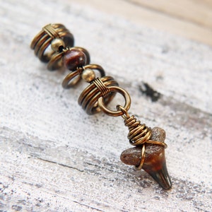 May include: A gold-toned hair wrap with a brown bead and a fossilised shark tooth pendant.