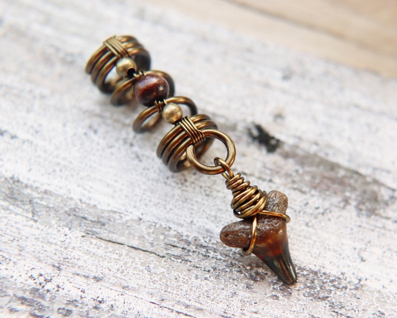 May include: A gold-toned hair wrap with a brown bead and a fossilised shark tooth pendant.
