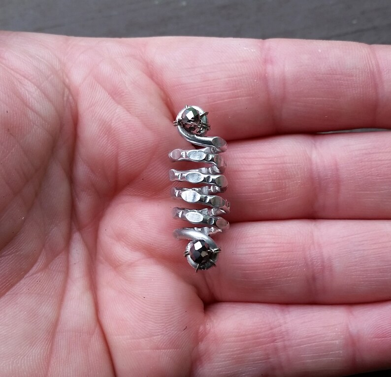 May include: A silver spiral ring with two black gemstones. The ring is made of metal and has a textured surface.