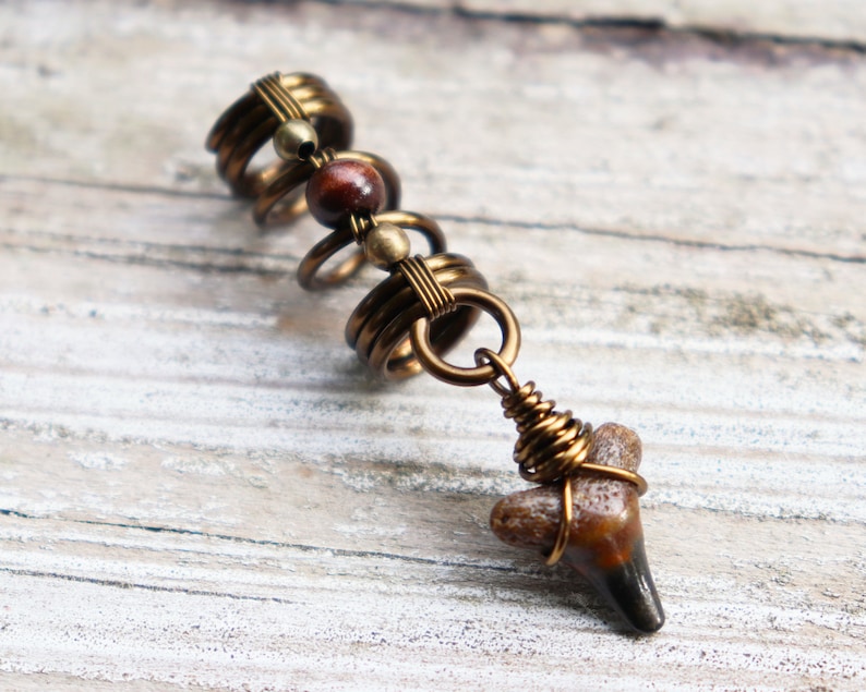 May include: A hair jewellery piece with a spiral of gold-toned metal rings and beads. A brown fossilised shark tooth hangs from the bottom of the spiral.