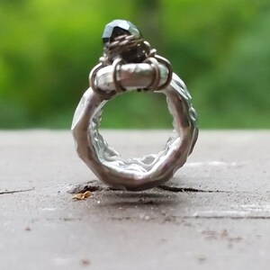 May include: A silver ring with a textured band and a dark green gemstone set in a wire cage.