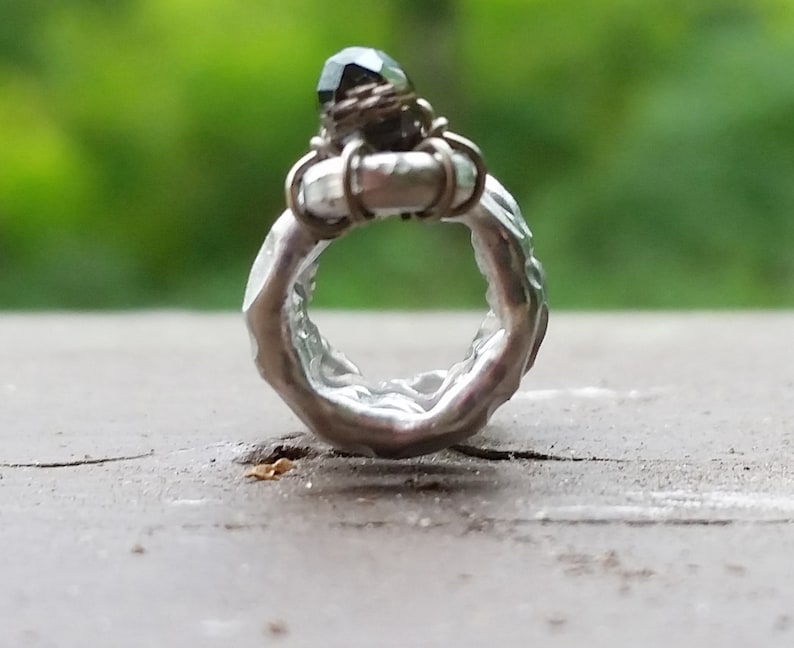 May include: A silver ring with a textured band and a dark green gemstone set in a wire cage.