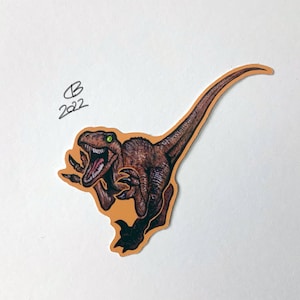 May include: A brown and green dinosaur sticker with a yellow background. The dinosaur is running and has its mouth open. The sticker has the text "B 2022" on it.