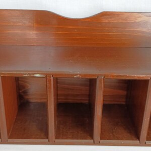 May include: A brown wooden storage unit featuring a flat top surface and five open rectangular compartments arranged side by side. The unit has curved side panels and a slightly arched backboard, showcasing a smooth, polished wood grain finish.