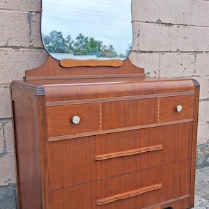May include: A wooden dresser featuring a warm brown finish, two small top drawers with clear glass knobs, and two larger lower drawers with long, textured wooden handles. A large, arched mirror is attached to the top of the dresser unit.