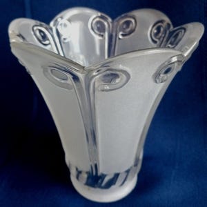 May include: A clear and frosted glass lamp shade featuring a scalloped, flower-like rim with raised swirl patterns. The glass transitions from a wide, fluted opening at the top to a narrower, circular base, showcasing a mix of smooth and textured surfaces.