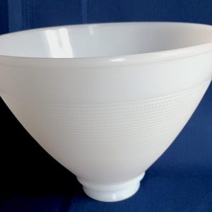 May include: A white milk glass lamp shade with a conical shape and a wide, open top. The exterior surface features a subtle, fine-textured grid pattern around the middle section, while the base narrows into a circular fitter for attachment.
