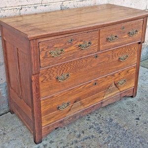 May include: A wooden dresser featuring a rectangular top and four drawers. The top row consists of two smaller drawers, while the bottom two rows feature full-width drawers. Each drawer is fitted with ornate brass handles and keyhole escutcheons.