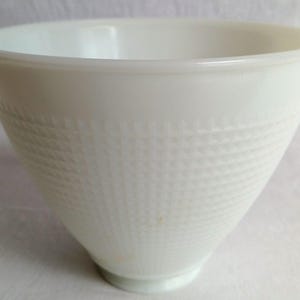May include: A white milk glass bowl with a wide, flared rim and a tapered base. The exterior surface features a textured, embossed grid pattern that covers the middle section of the bowl, while the top rim remains smooth and plain in appearance.