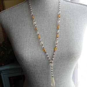 Peut inclure: Un long collier de perles avec des perles de verre transparentes et ambr&eacute;es. Le collier a un pendentif en forme de larme au bas.