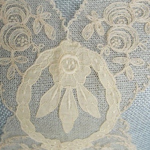 May include: Close-up of a delicate white lace fabric with a floral design. The lace features intricate details, including small flowers and leaves.