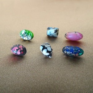 May include: Six colourful glass beads with various patterns, including pink, green, blue, black and white.